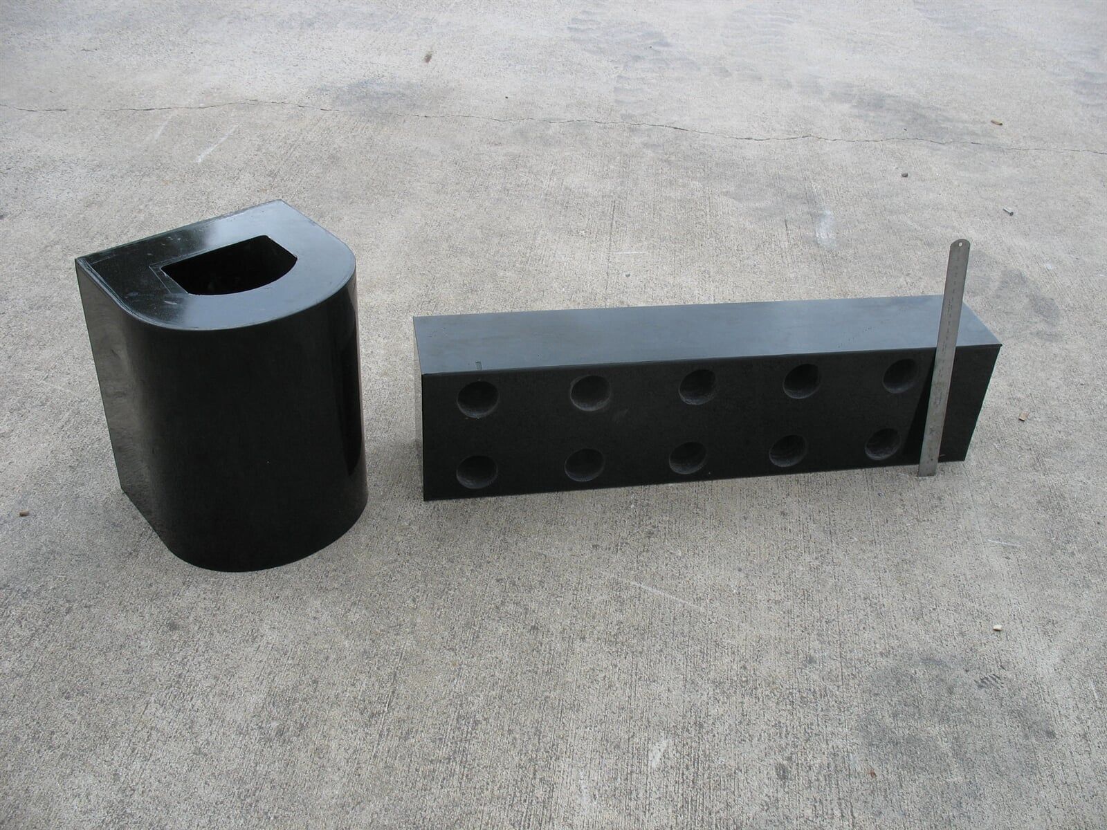 Two black blocks with holes in them are on a concrete surface - Engineering Tooling In Thornton, NSW