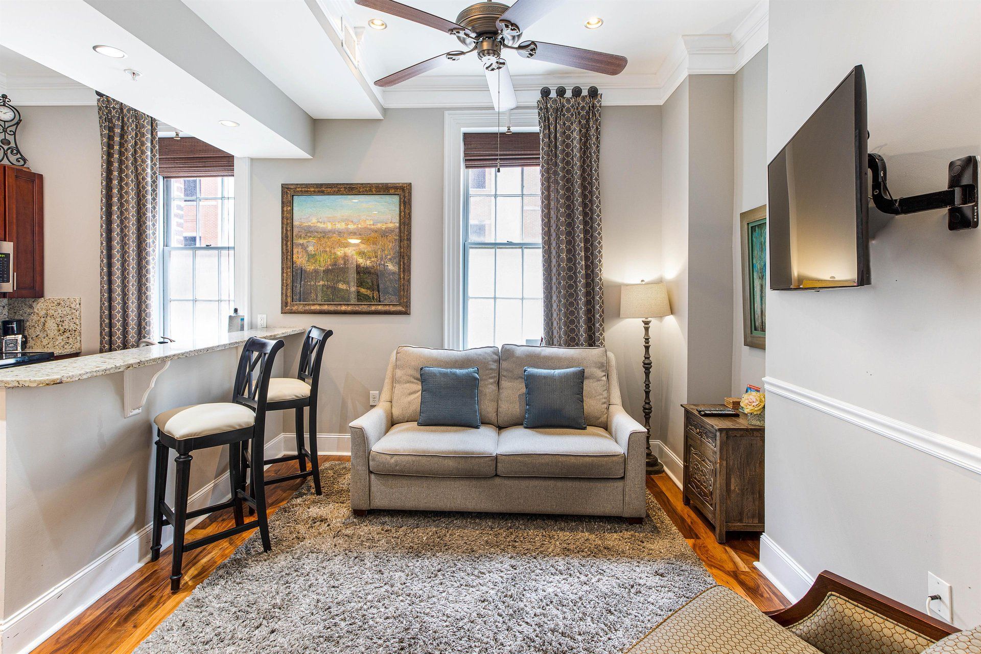 Cozy living room with sofa, bar, and mounted TV. Neutral tones, windows, and decorative accents.