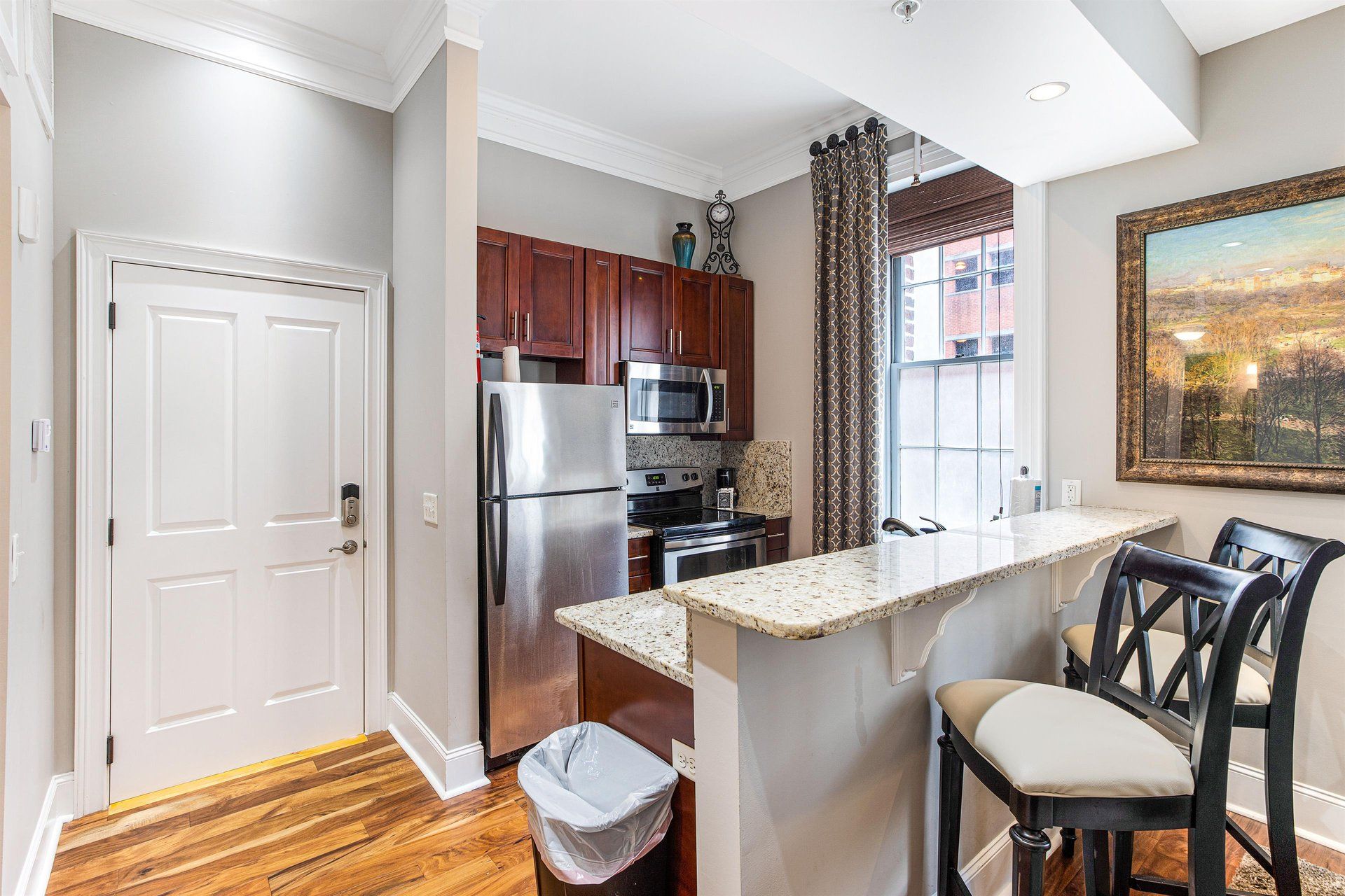 Kitchen with stainless steel appliances, breakfast bar, hardwood floor, and a framed painting.