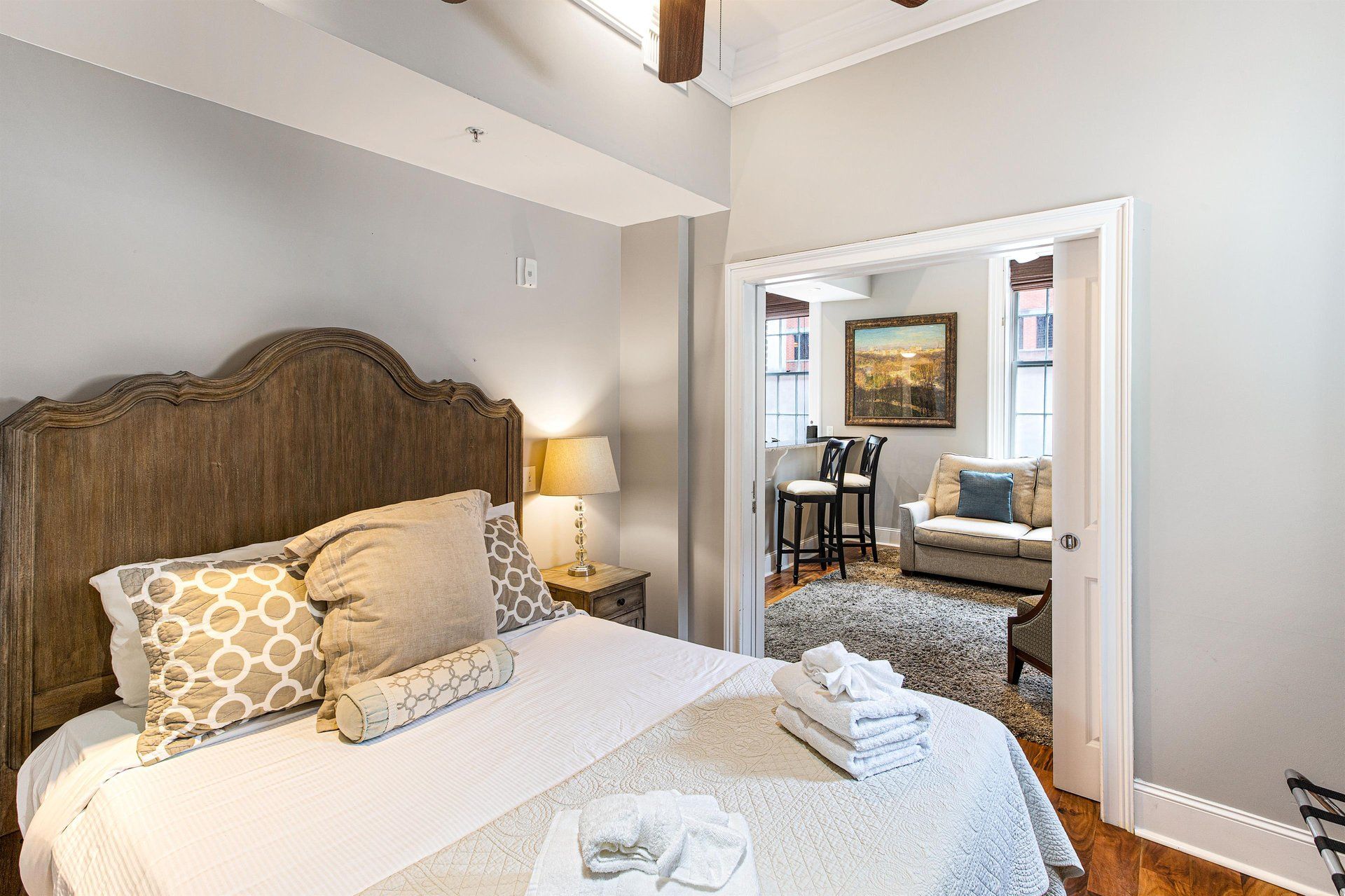 Bedroom with bed, pillows, and a doorway leading to a living area with furniture and artwork.