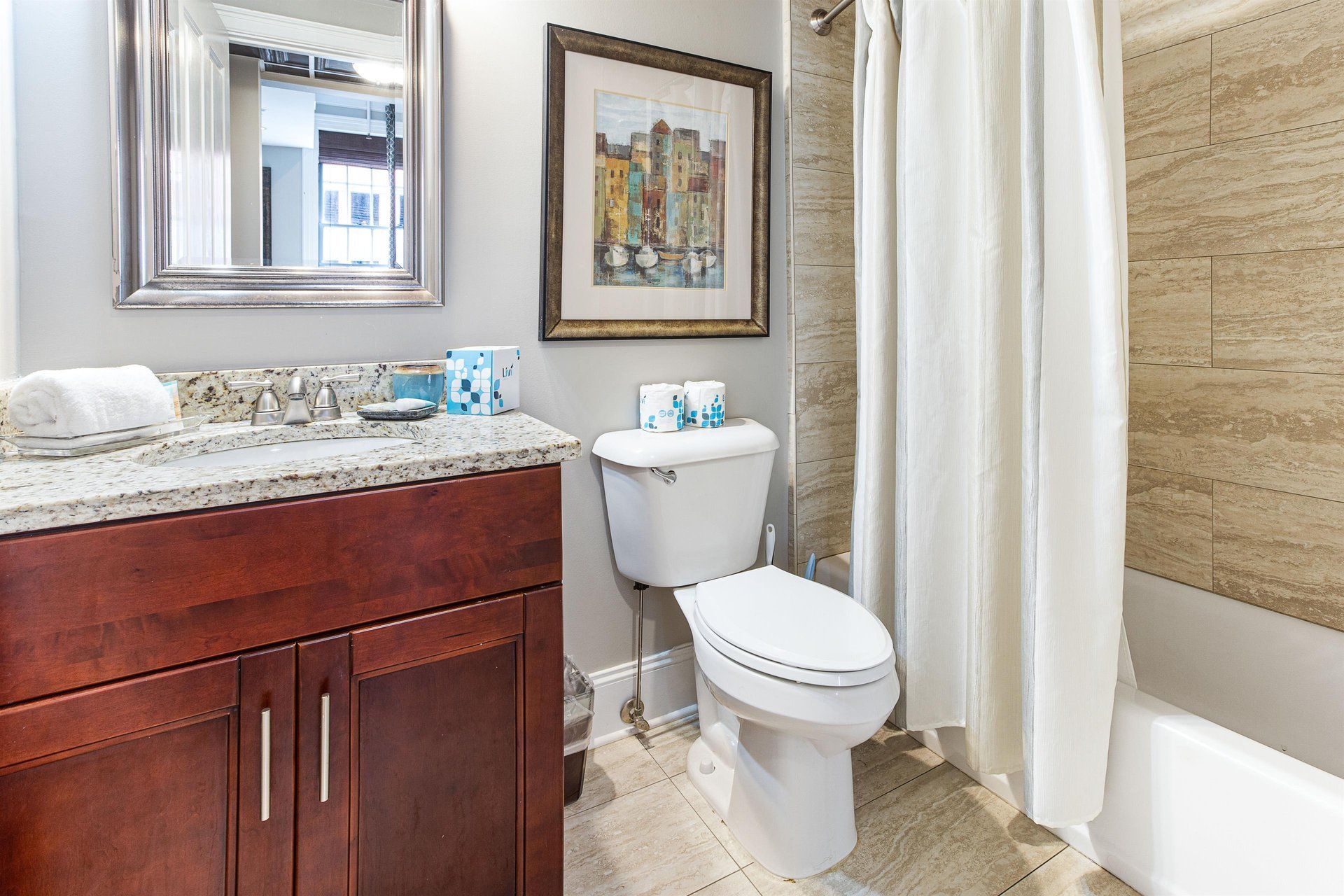 Bathroom with vanity, toilet, and bathtub/shower. Neutral tones, artwork on wall.