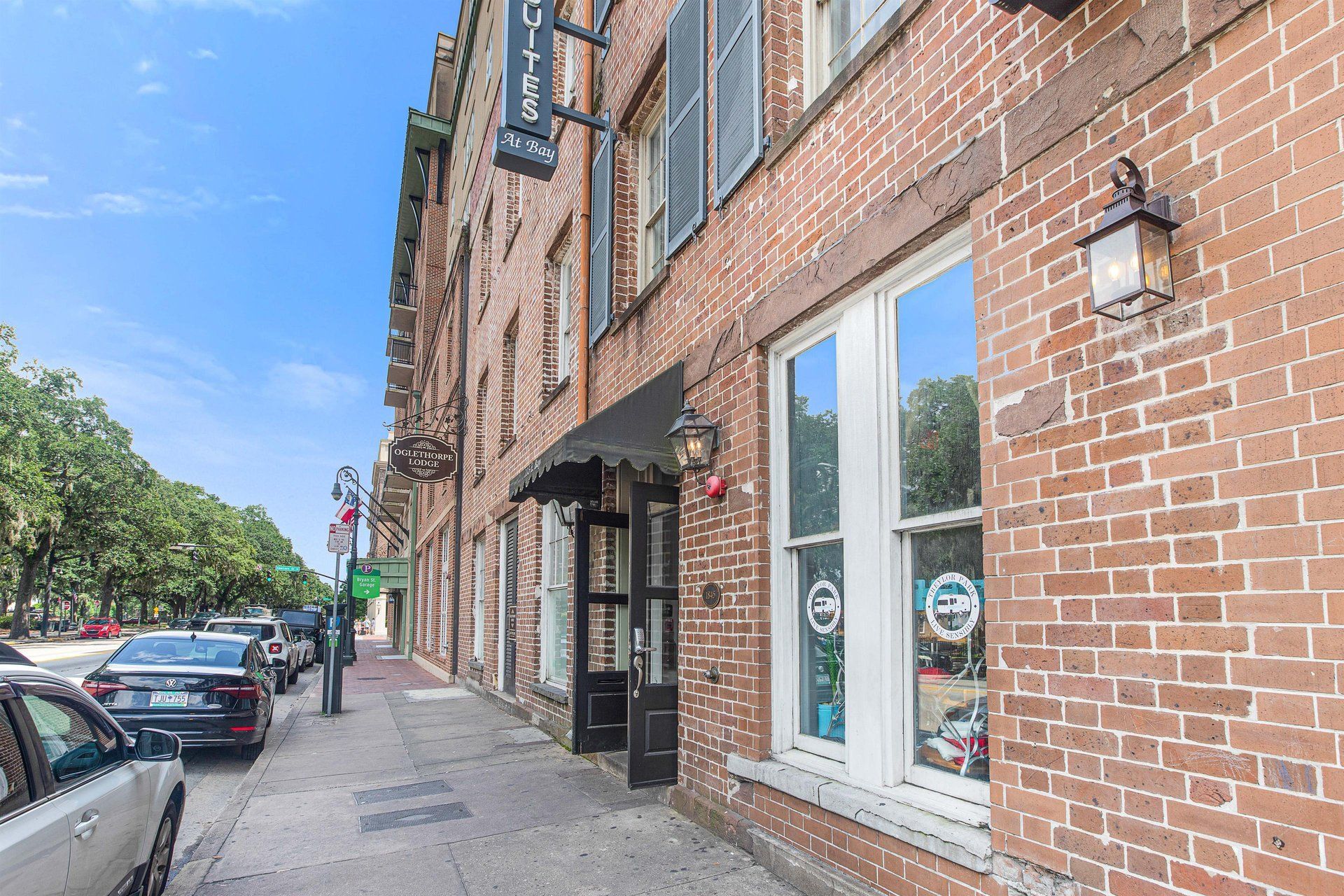 Brick building with storefronts on a city street. Cars are parked along the sidewalk.