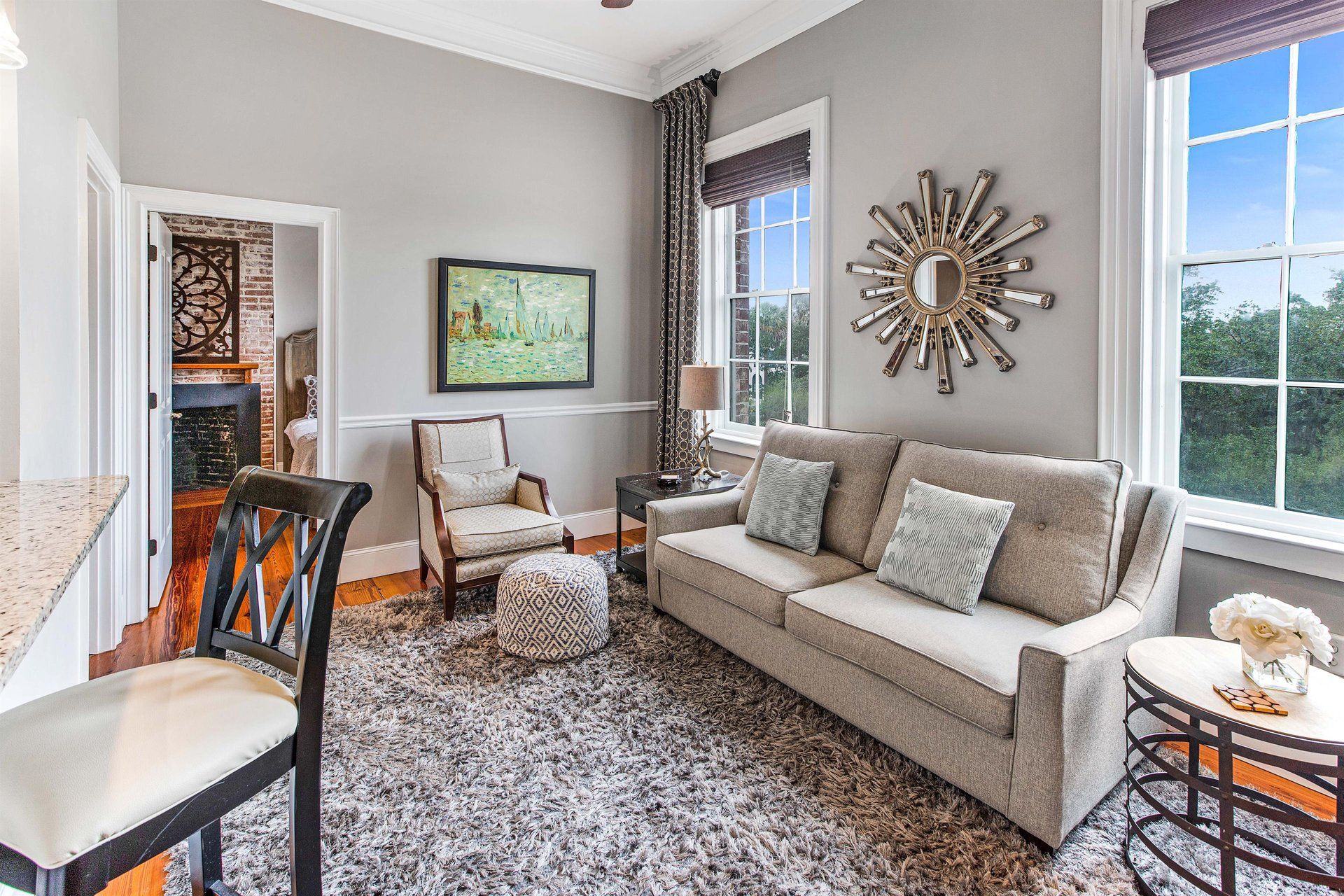 Living room with gray walls, beige sofa, armchair, patterned rug, and sunburst mirror.