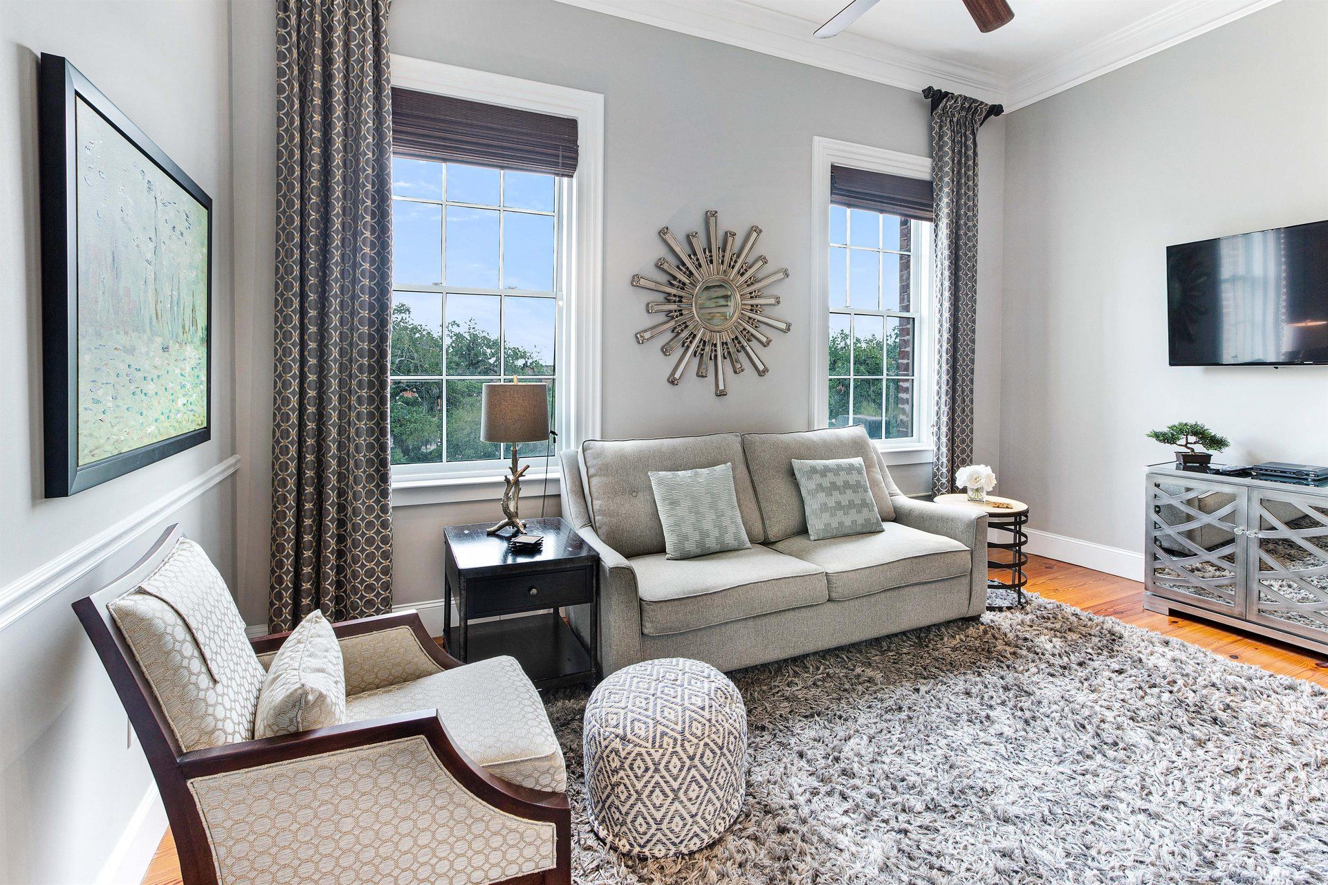 Living room with gray walls, sofa, chair, windows, rug, TV, and decorative accents.