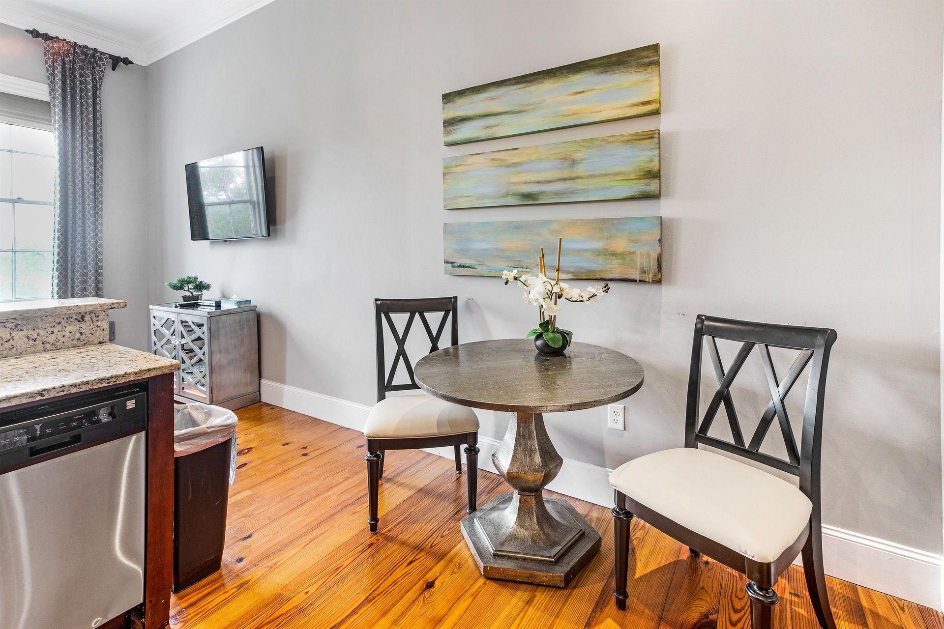 Small dining area with table and two chairs, art, TV on wall, and hardwood floors.