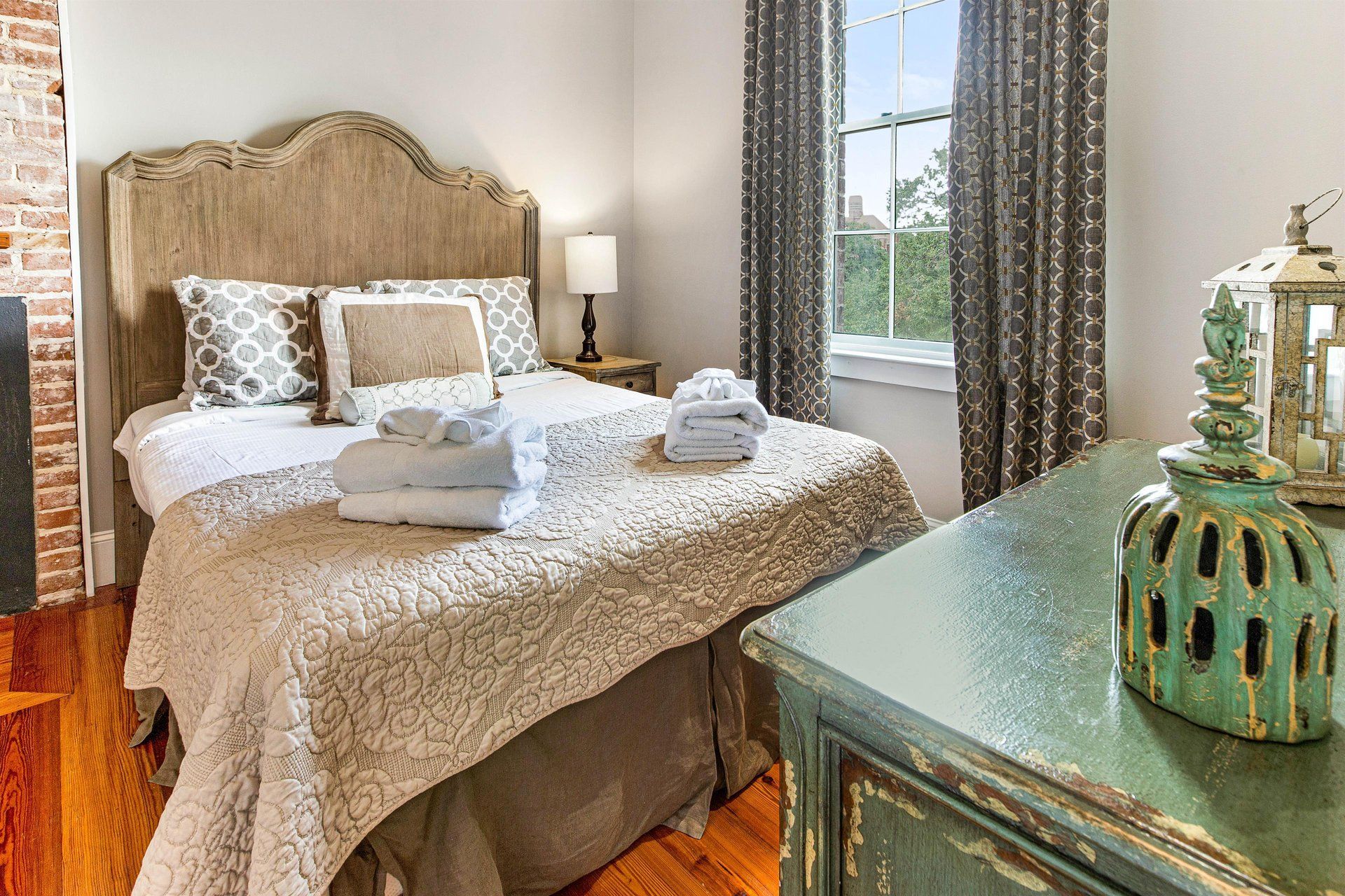 Cozy bedroom with bed, bedside table, window with curtains, and turquoise dresser.
