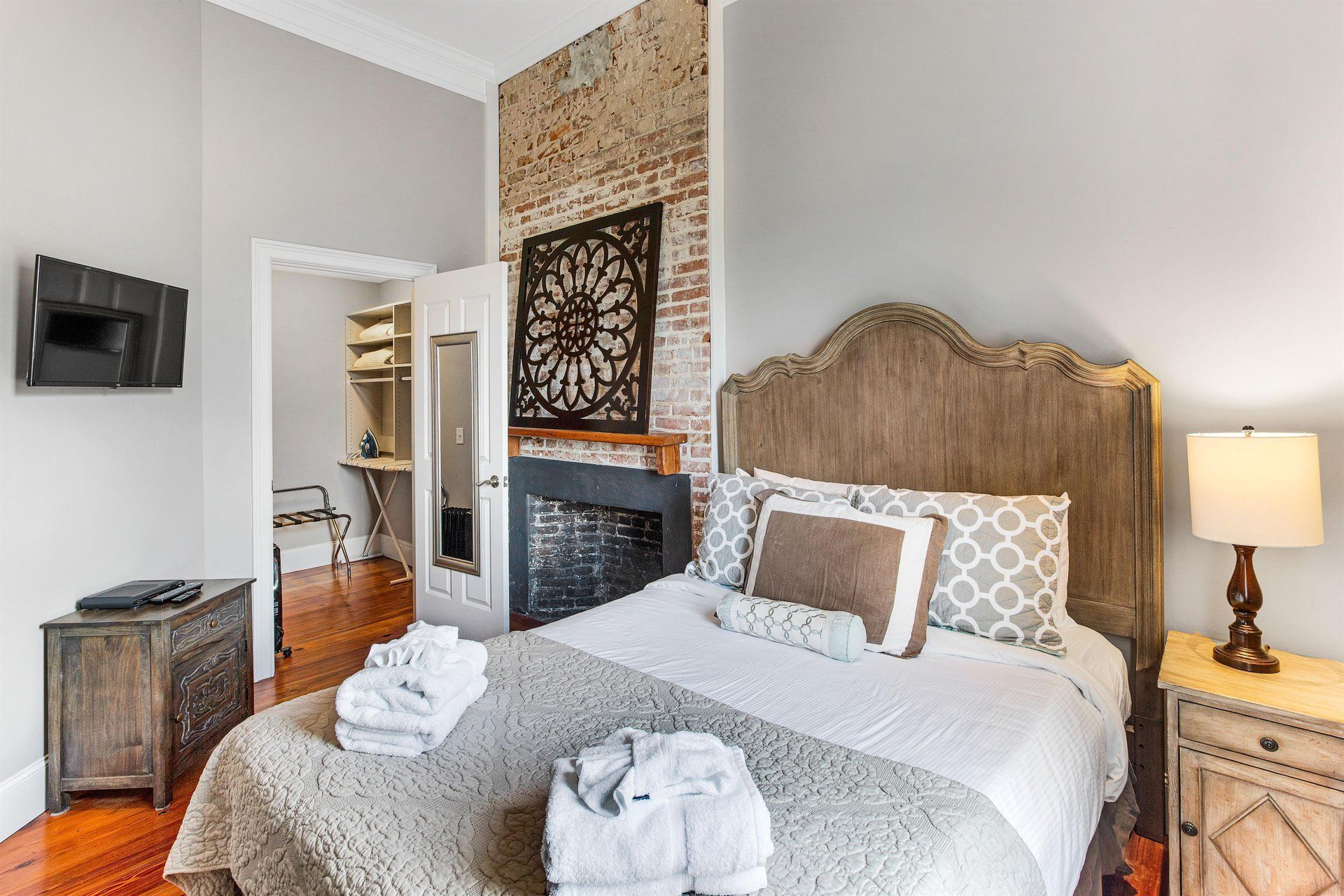 Bedroom with bed, exposed brick fireplace, nightstand, and small TV on wall.