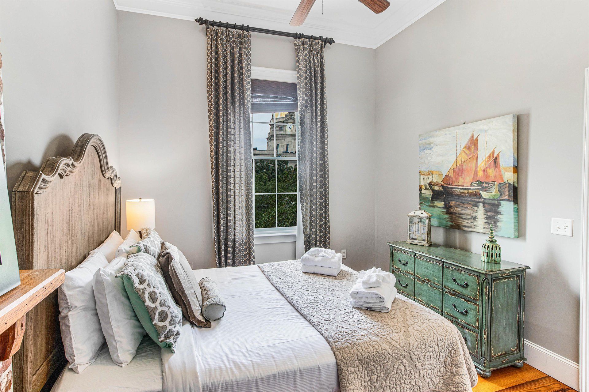 Bedroom with a wooden headboard, turquoise dresser, and a window with curtains.