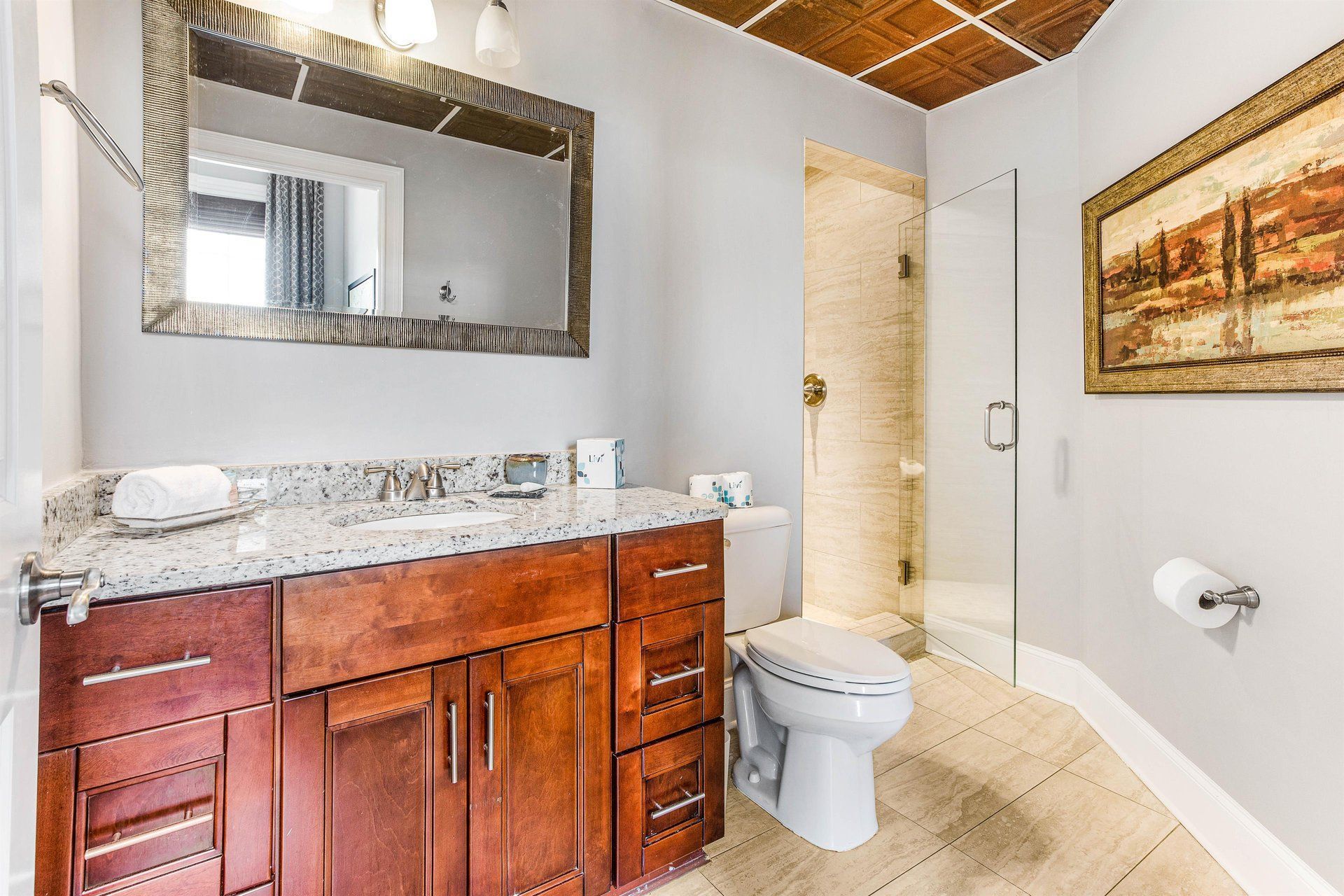 Bathroom with a vanity, toilet, glass shower, art, and a decorative ceiling.