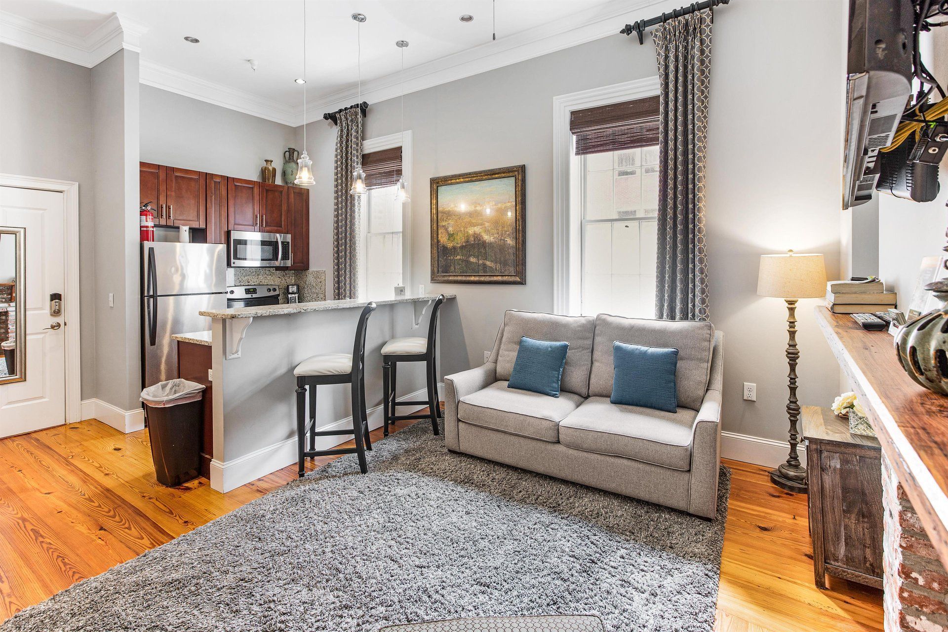Small living space with kitchen, sofa, rug, and windows; gray walls and wooden floors.