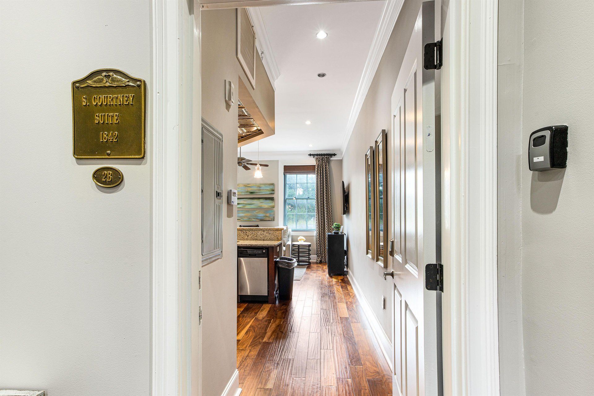 Hallway view, looking toward a kitchen. Wooden floors, white walls, gold sign on the left.