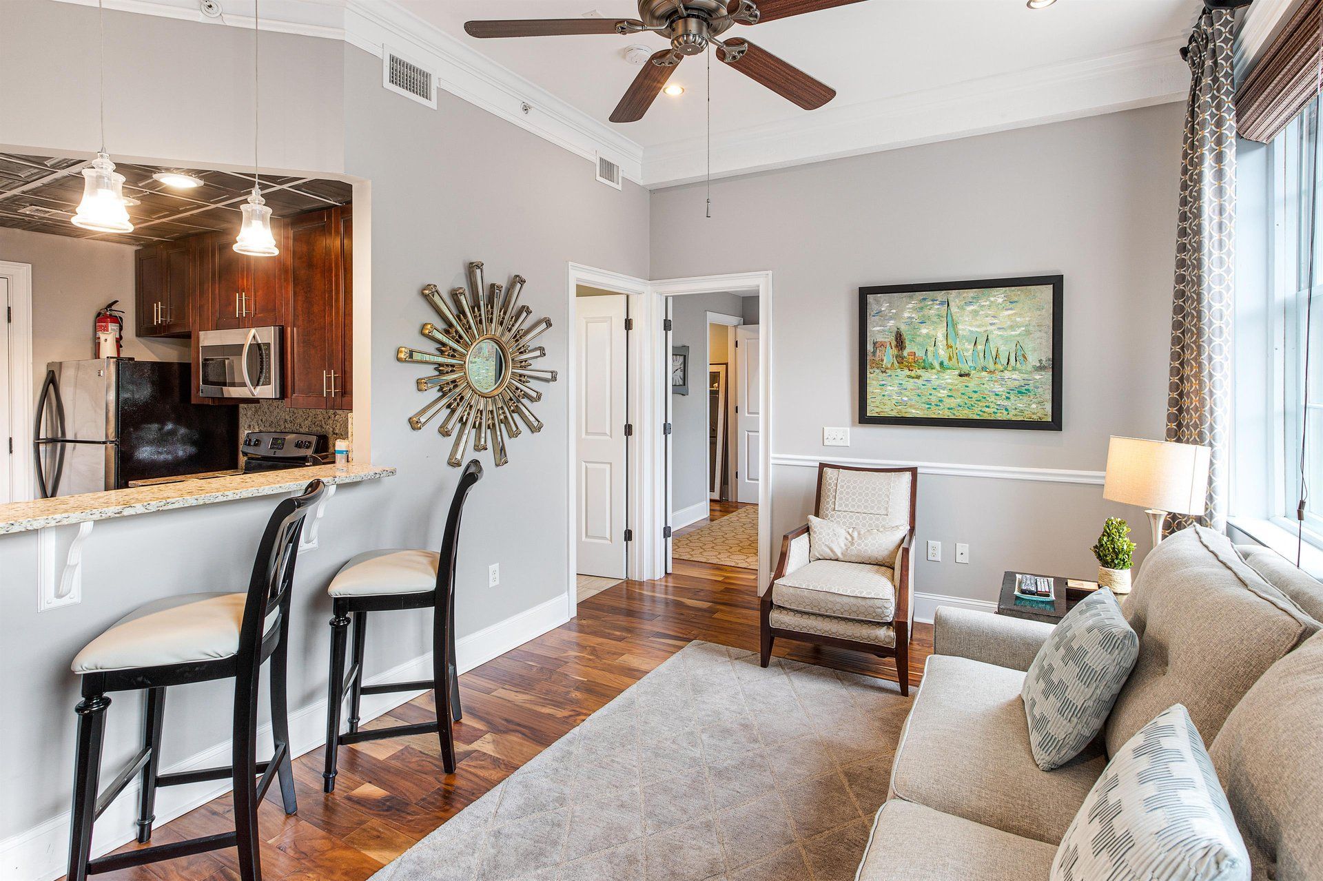 Living room with bar seating, open kitchen, sofa, armchair, and artwork.