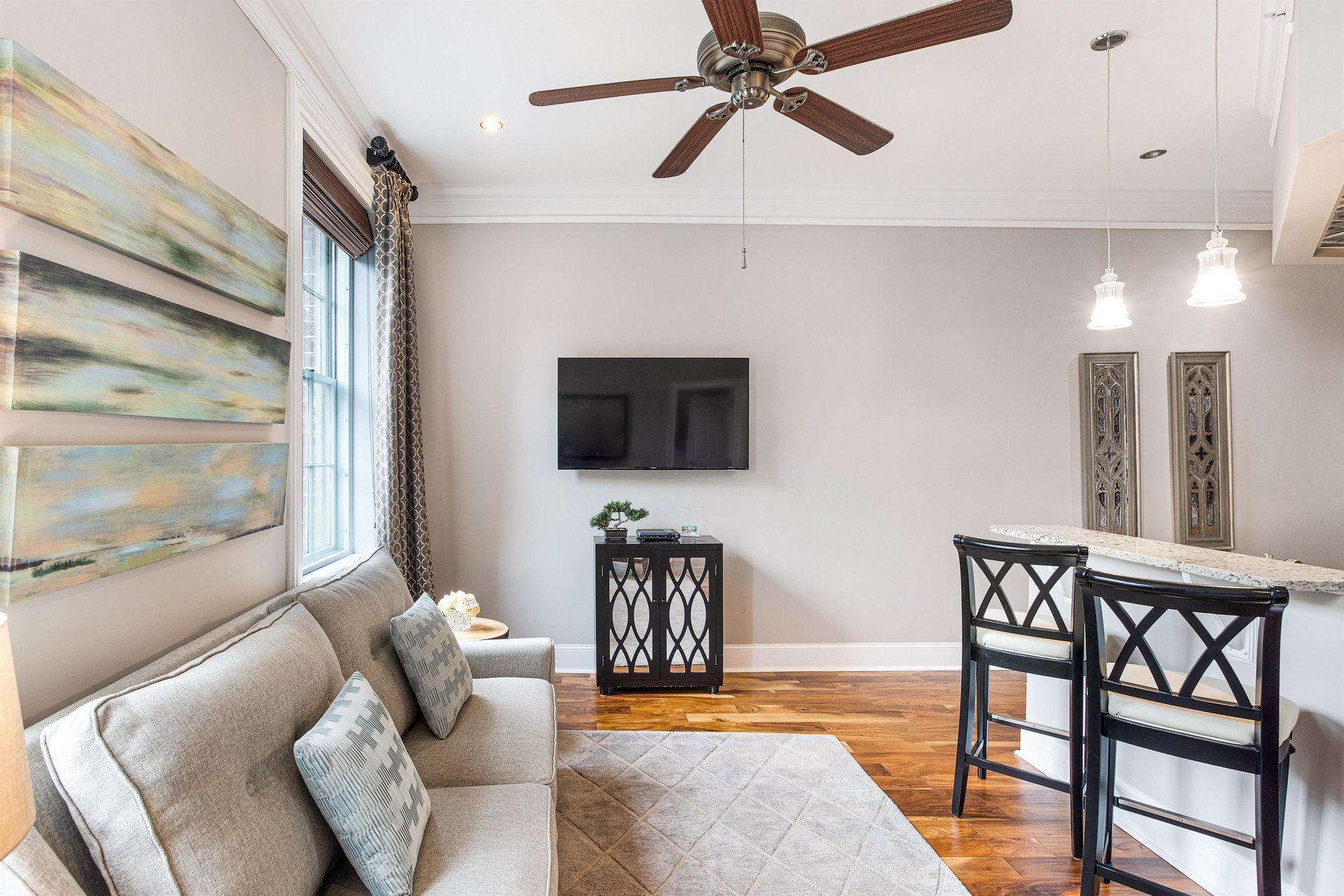 Cozy living space with sofa, TV, and breakfast bar. Neutral walls, wooden floor, artwork and ceiling fan.