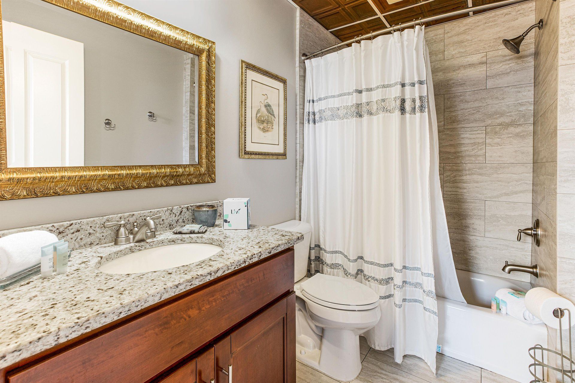Bathroom with white and gray marble, a dark wood vanity, and gold-framed mirror.