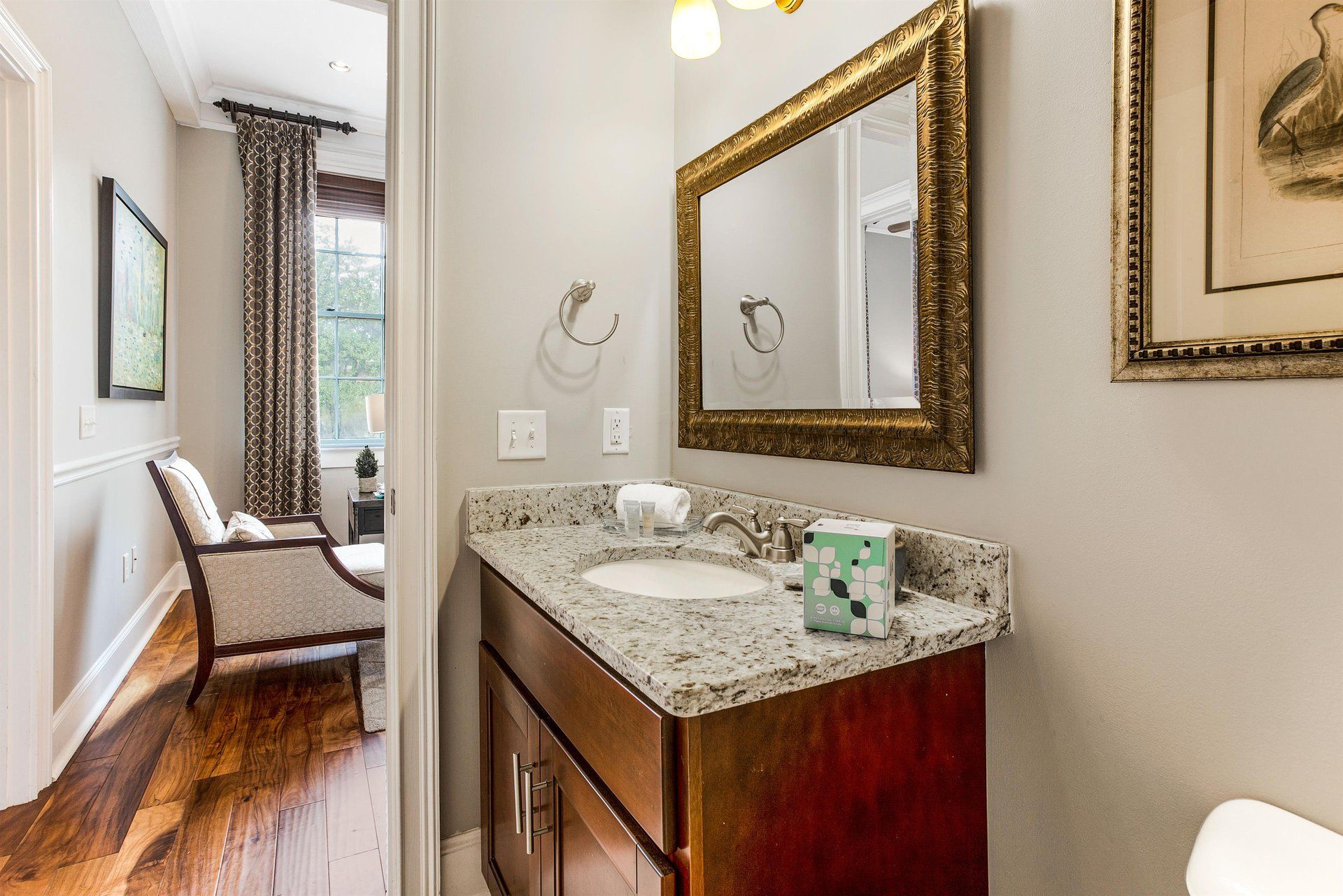 Bathroom with marble countertop, ornate mirror, and doorway to a sitting area with a chair.