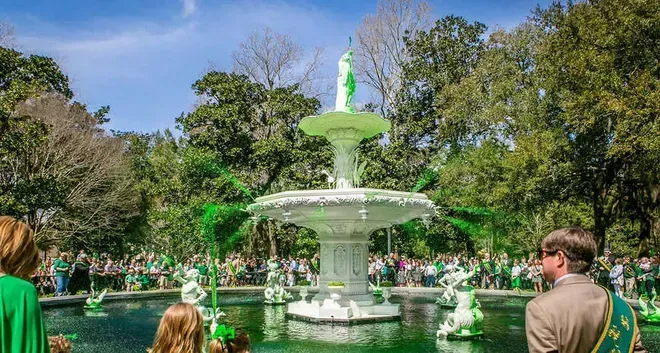 Fountain in Forsyth Park, Savannah, dyed green for St. Patrick's Day, surrounded by spectators on a sunny day.