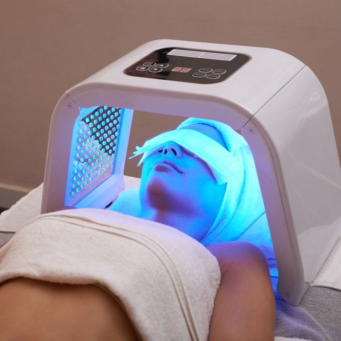Woman undergoing blue LED light therapy, eyes covered, in a spa setting.
