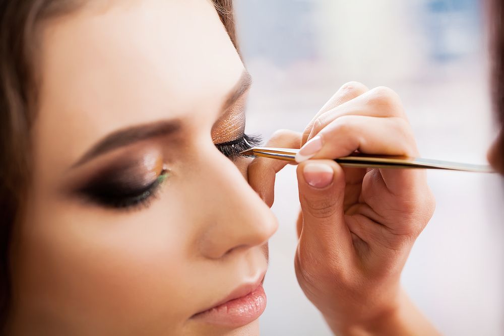 Person getting false eyelashes applied by makeup artist.