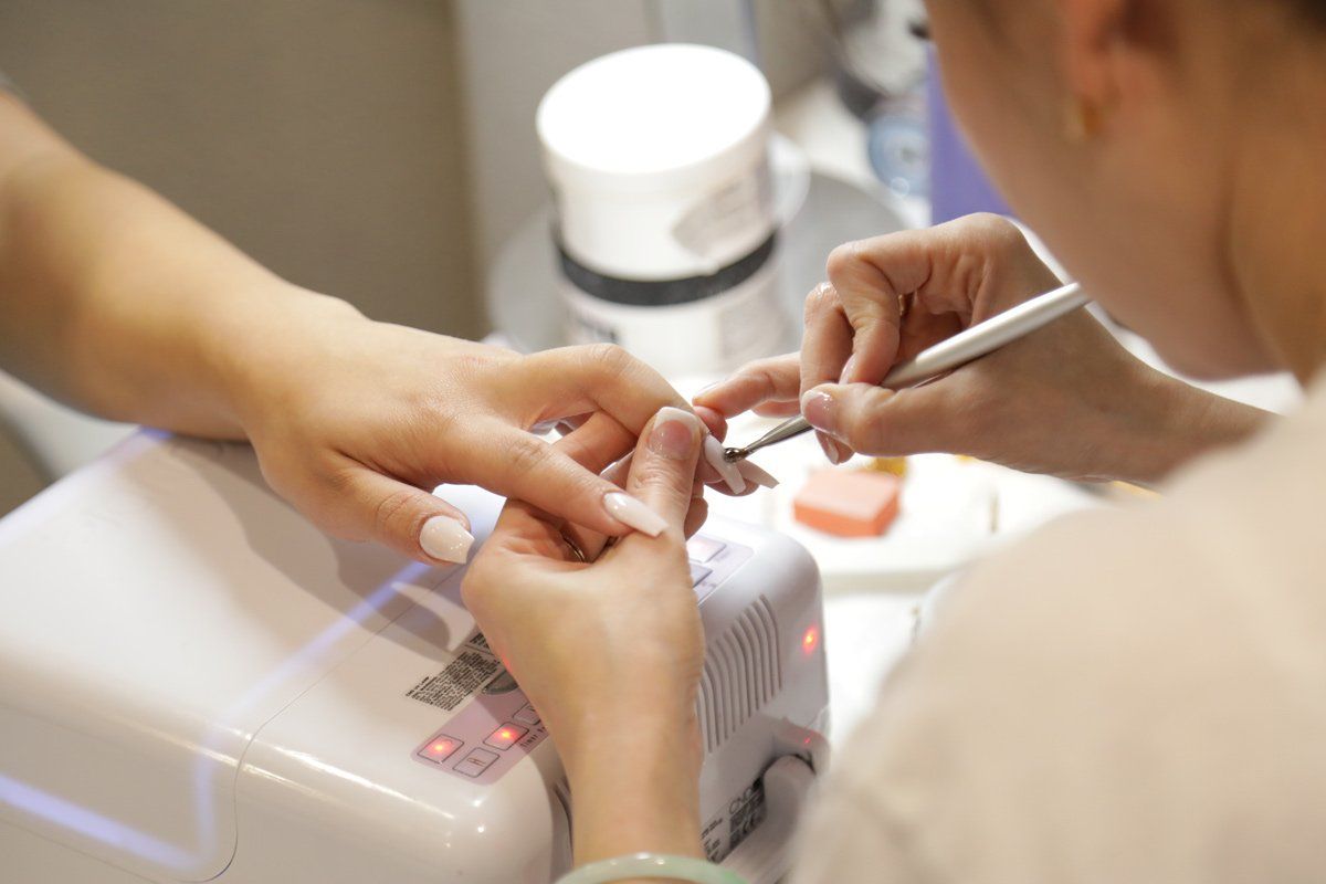 A person receiving a manicure, hand being worked on with tools by a technician in a salon setting.