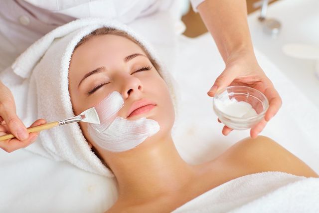 Woman receiving a facial mask treatment at a spa; a therapist applies mask to her face.
