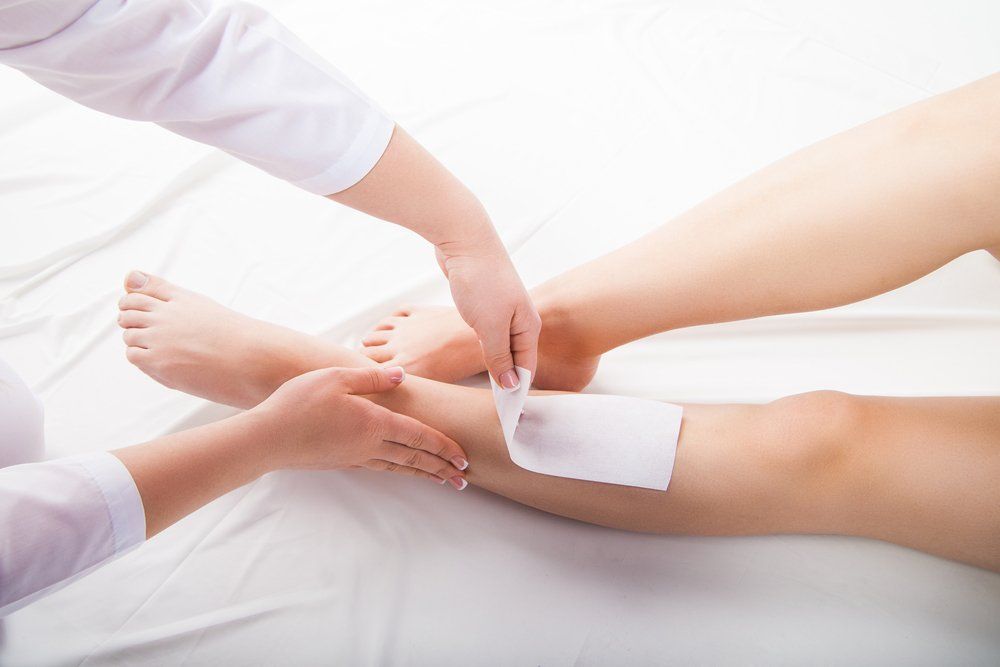 A person's leg being waxed by a person in a white coat.