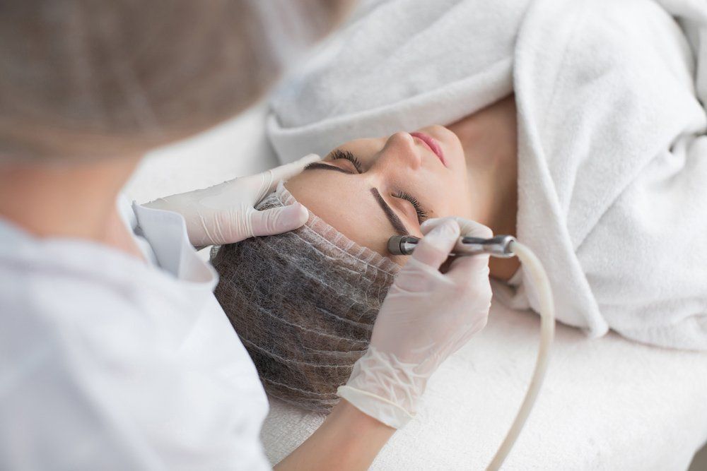 A woman receiving a facial treatment at a spa. A gloved esthetician uses a tool on her face.
