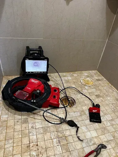 Drain inspection equipment in a shower. A monitor displays the drain's interior. A red camera reel and tools are present.