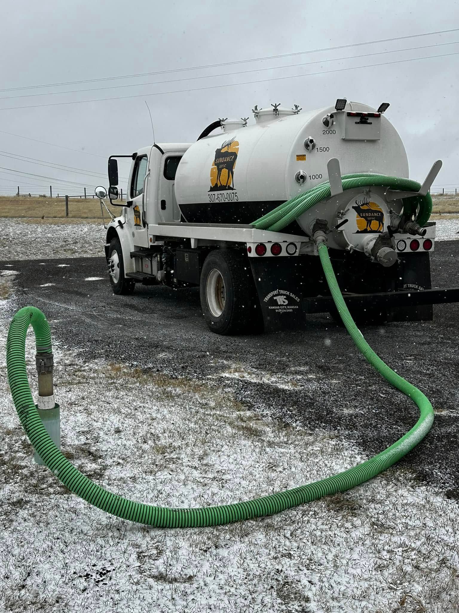 White septic tank truck with green hose, parked outside on a snowy day.