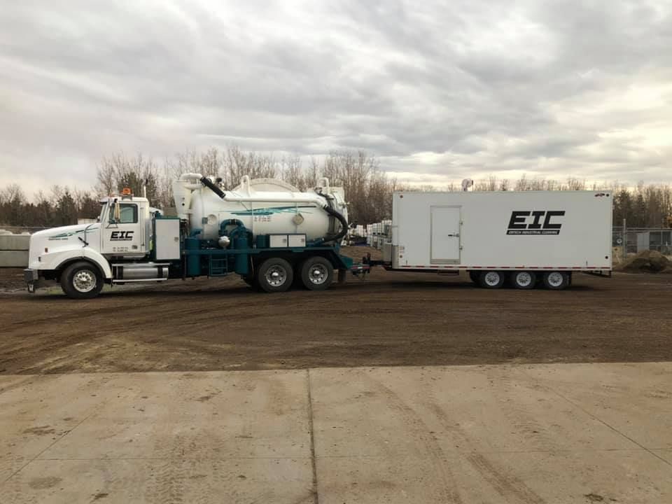 A vacuum truck with a trailer attached to it is parked in a parking lot.