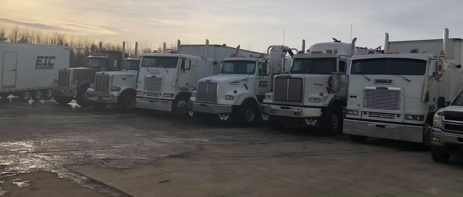 A row of semi trucks are parked in a parking lot.