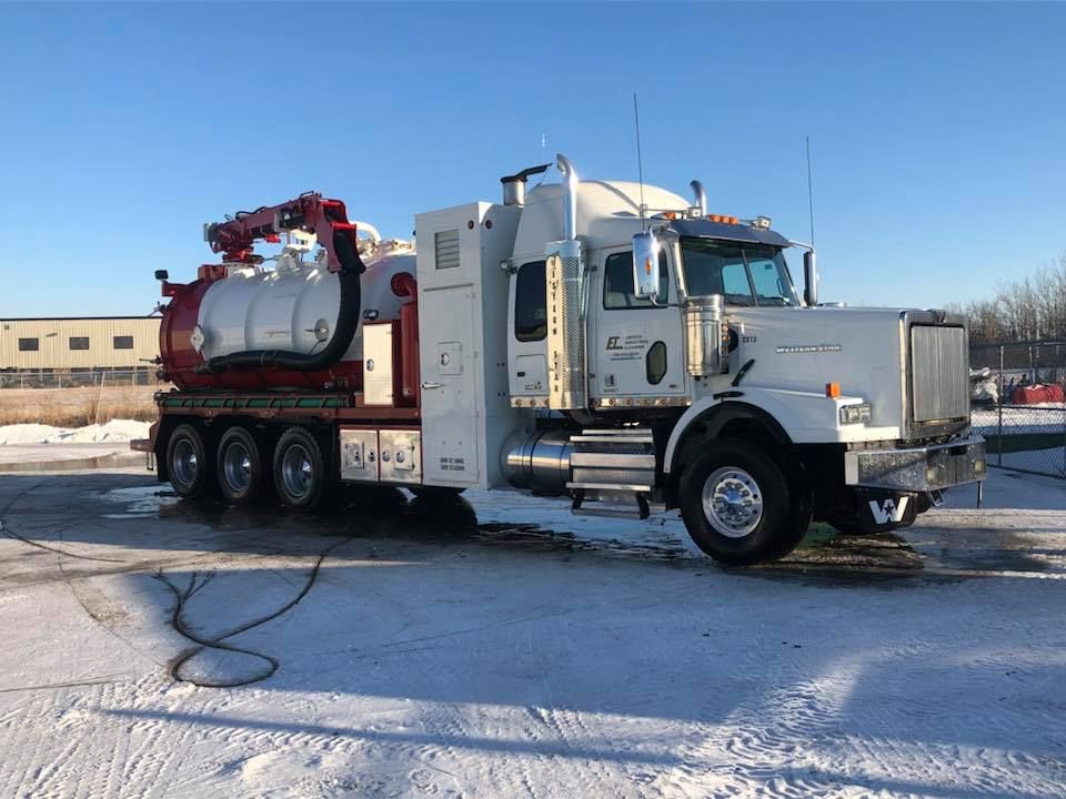 A white and red vacuum truck is parked in the snow.