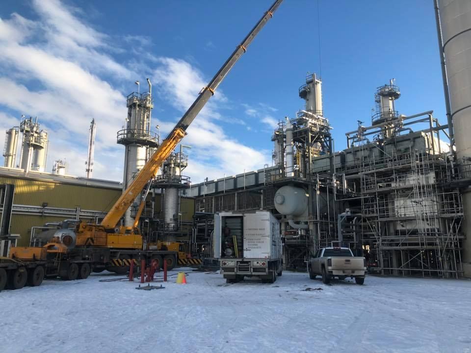 A large yellow crane is sitting in front of a large industrial building.