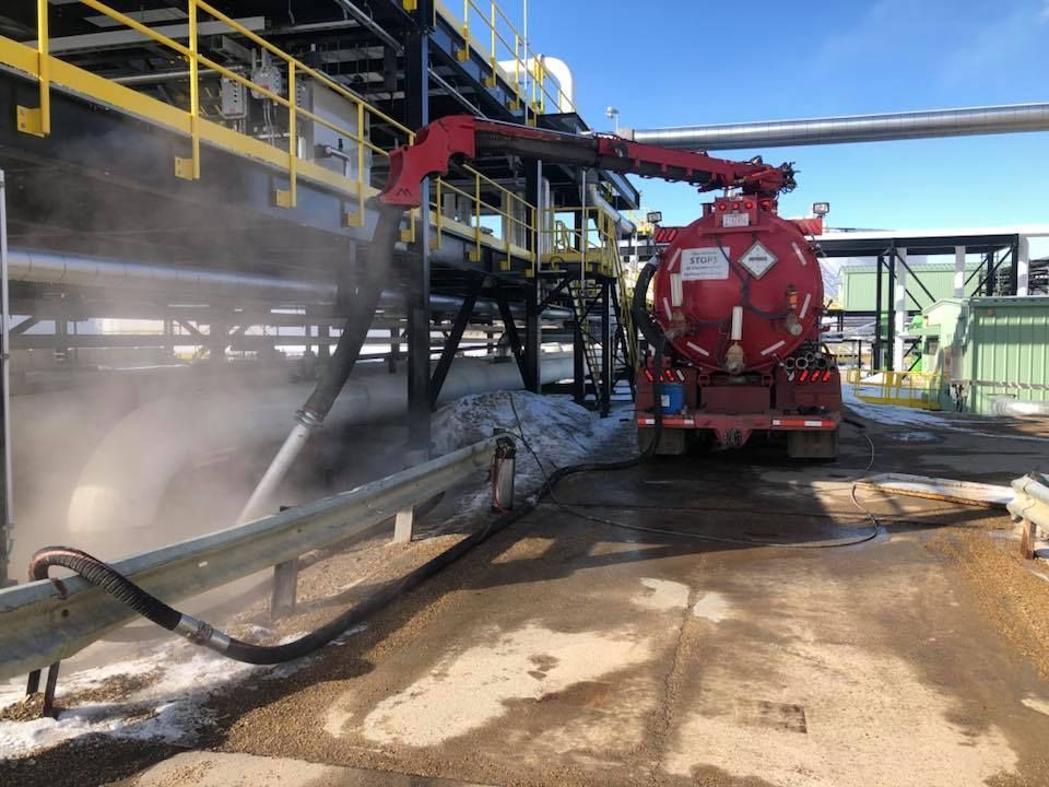 A red vacuum truck is cleaning a pipe in a factory.