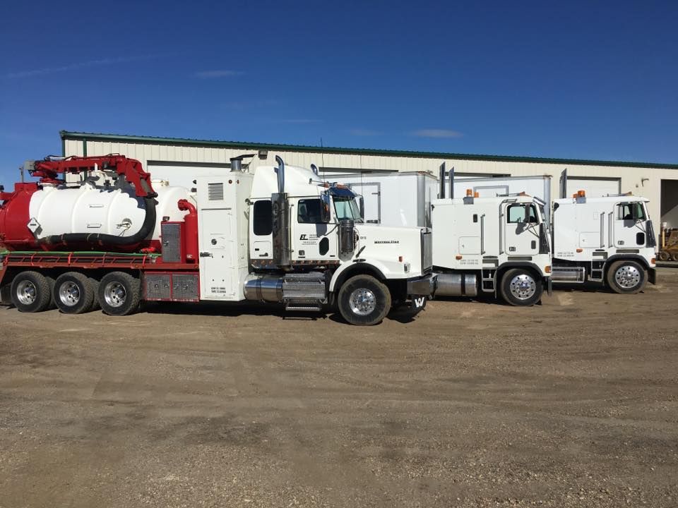 Three semi trucks are parked in a lot in front of a building.