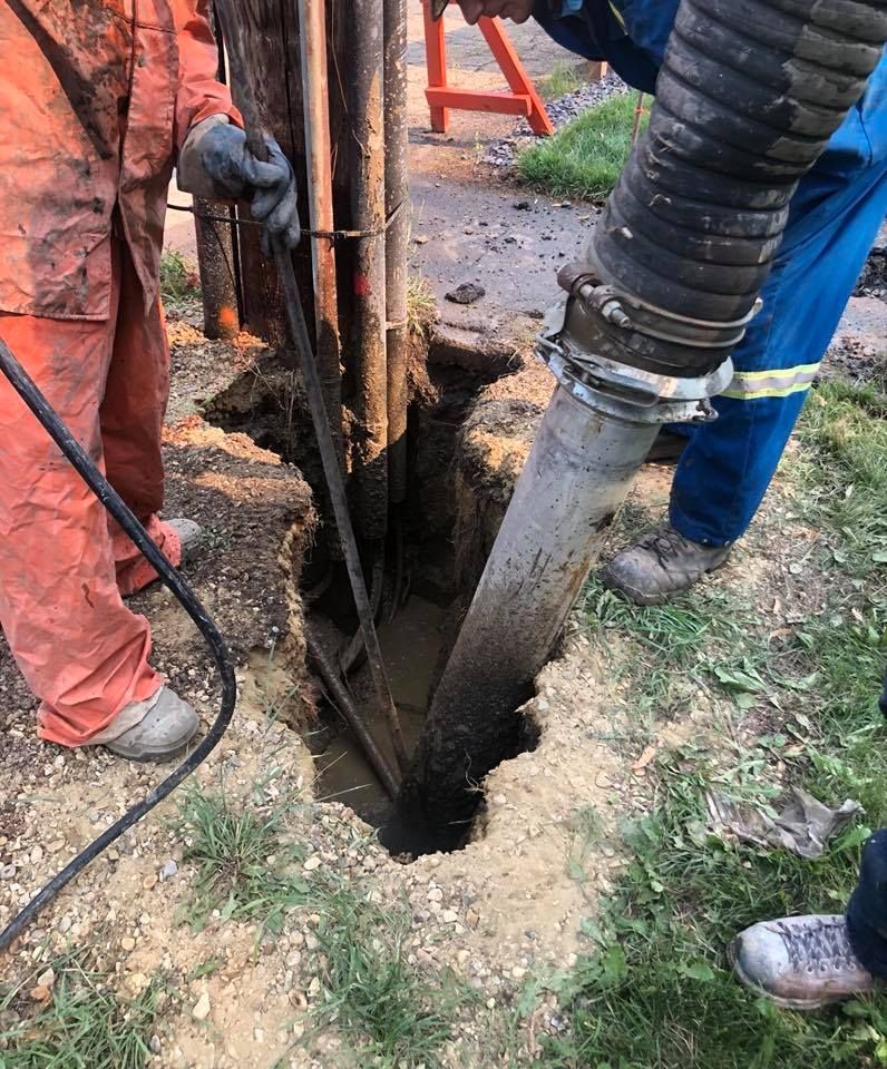 A man is using a hose to pump water into a hole in the ground.