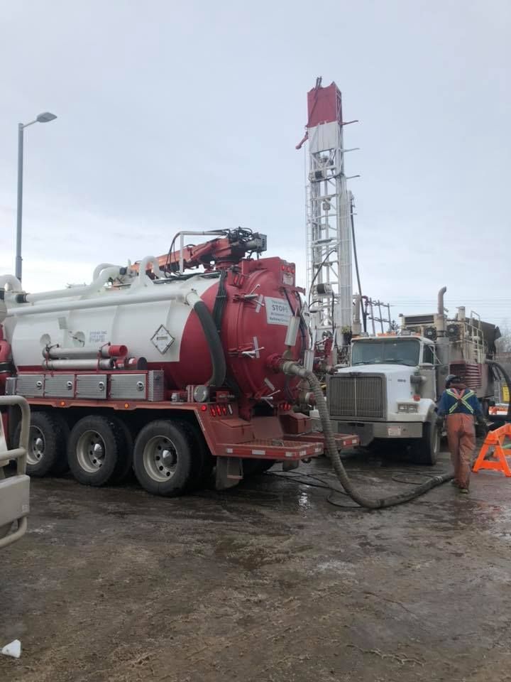 A red and white vacuum truck is parked next to a white truck.