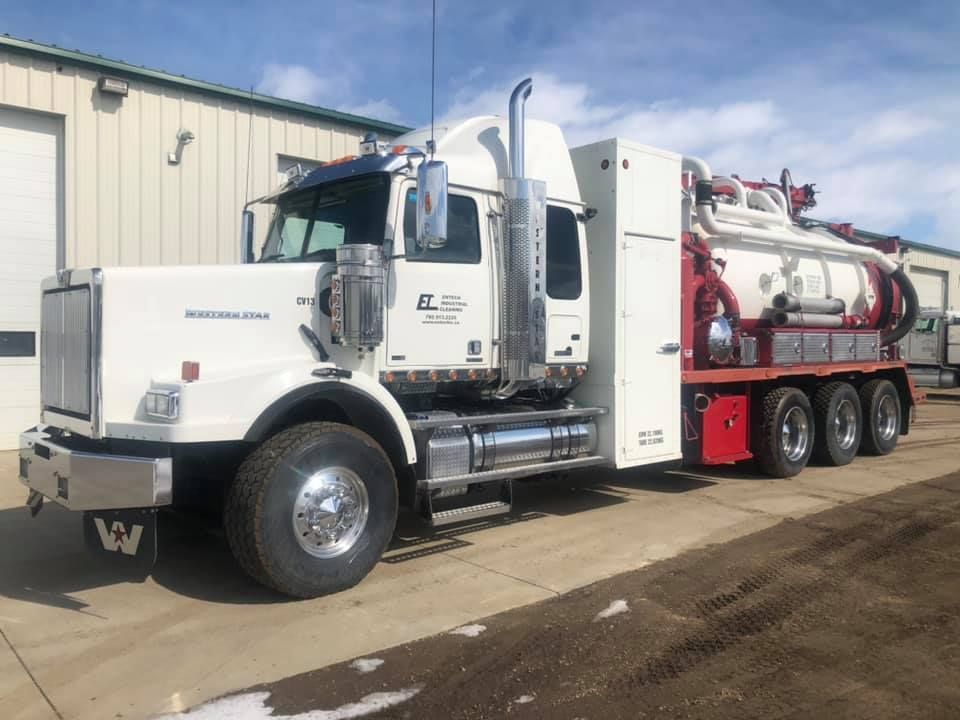 A white semi truck with a red trailer is parked in front of a building.