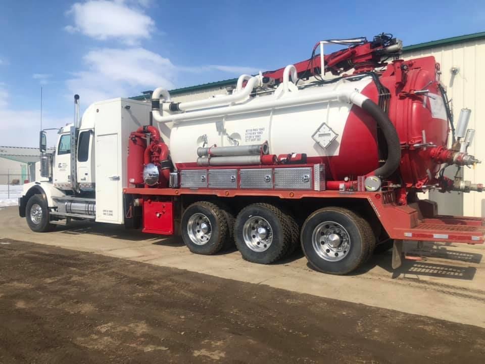A red and white vacuum truck is parked in front of a building.