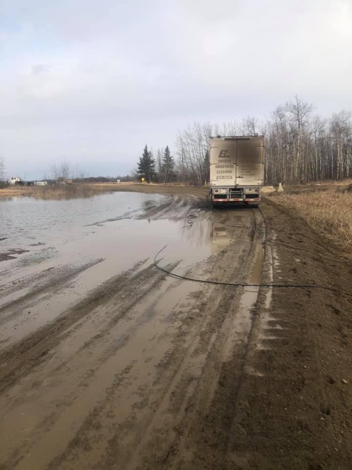 A truck is driving down a muddy road next to a body of water.