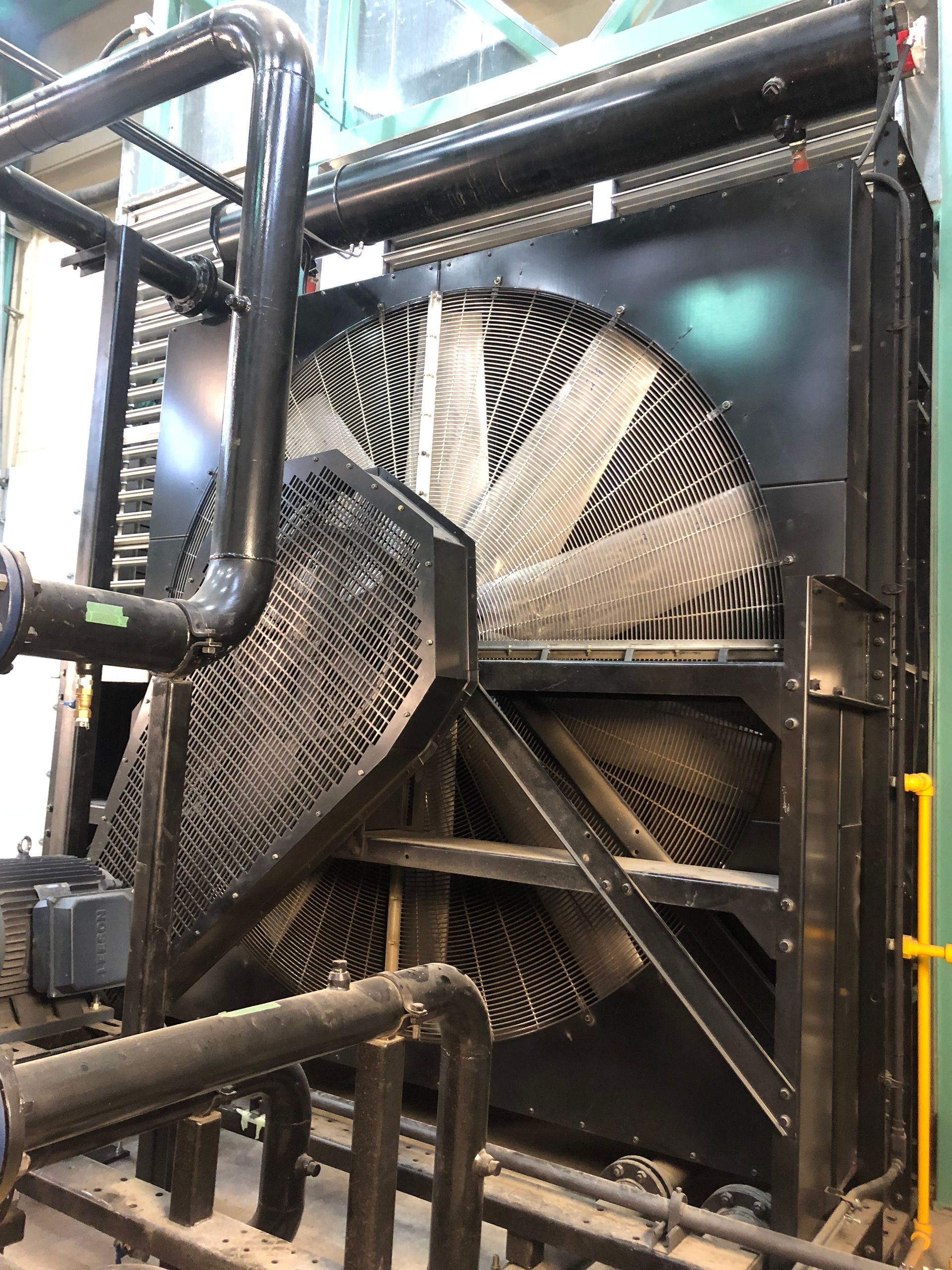A large fan is sitting in a room next to pipes.