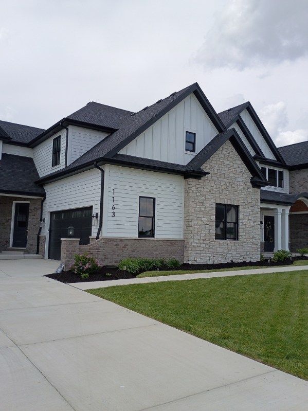Modern gray-and-white suburban house with a driveway and green lawn under cloudy skies