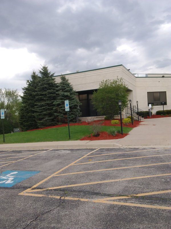 Parking lot outside a beige building with trees, red mulch, and cloudy sky
