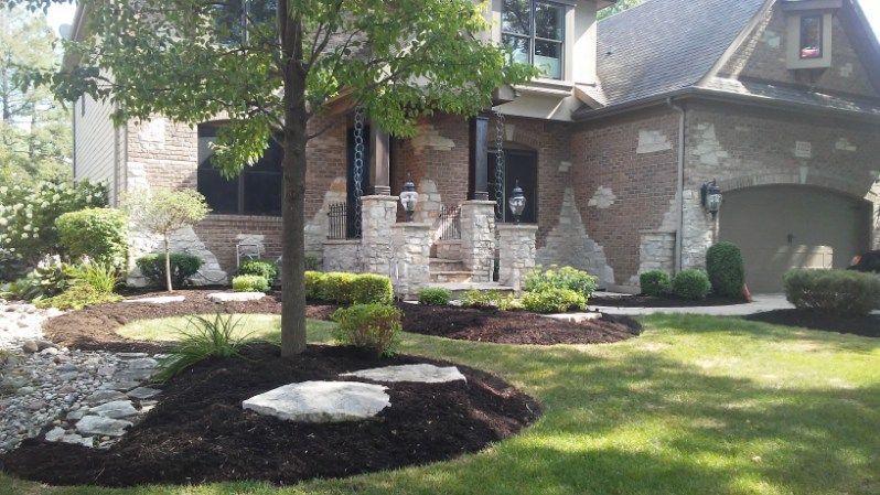 Landscaped brick house with a tree, shrubs, and a green lawn in the front yard