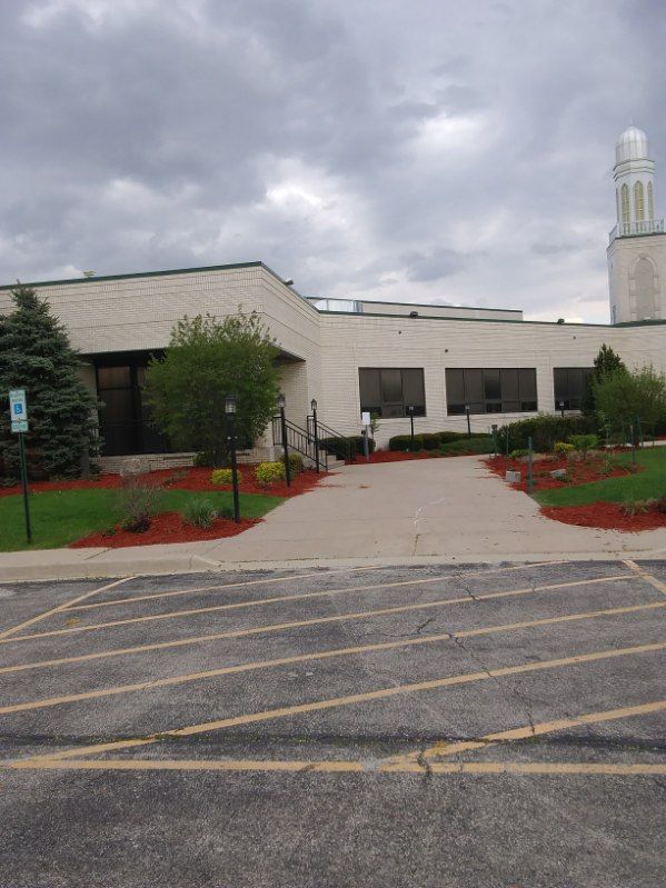 Low beige building with landscaped entrance under a cloudy sky, viewed from a parking lot.