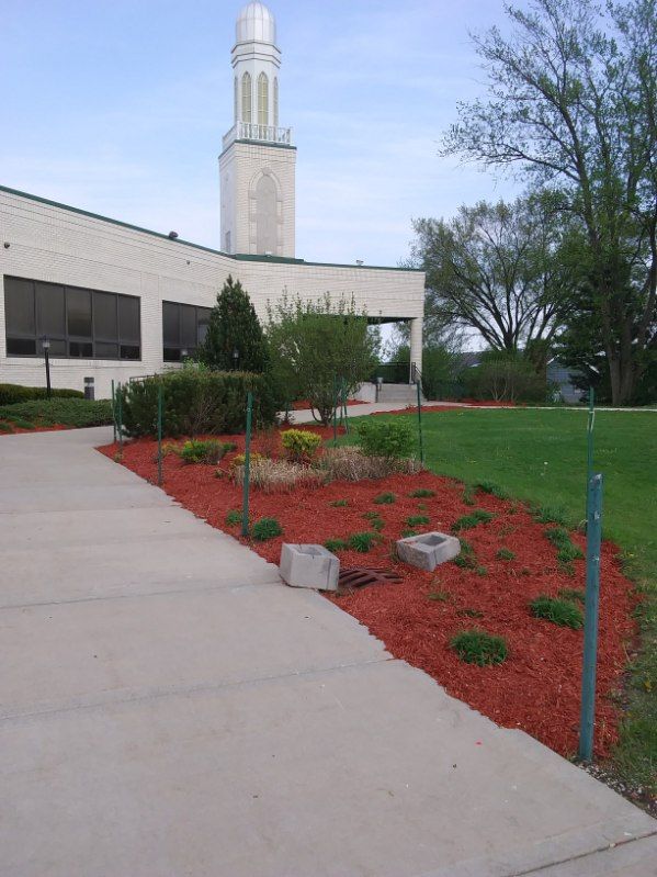 Landscaped walkway with red mulch, shrubs, and a tall tower beside a beige building