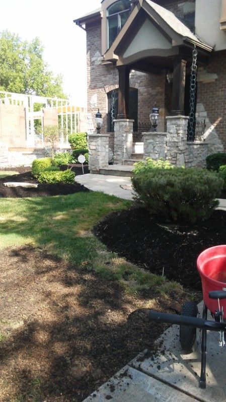 Front yard with a stone porch, trimmed shrubs, and a red chair on a sunny day