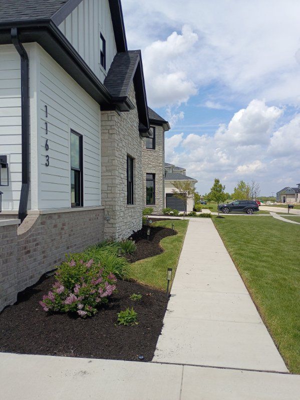 Sidewalk beside a house with landscaped flower beds and green lawn under a cloudy sky