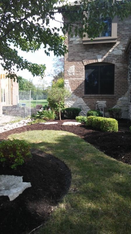 Landscaped garden beside a stone building with arched window, trees, shrubs, and a grassy lawn