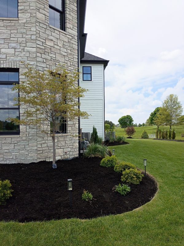 Stone and white house exterior with landscaped shrubs, lawn, and a small tree beside a clear sky.
