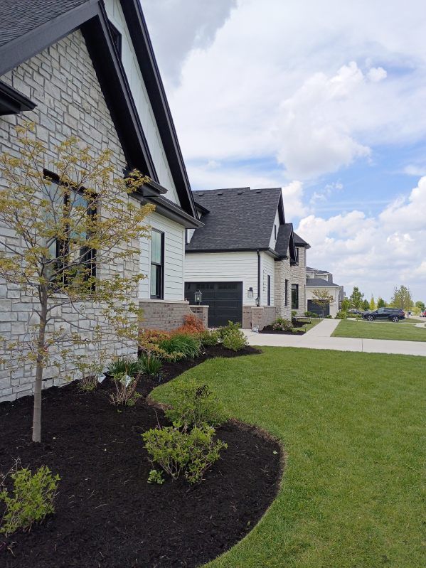Suburban homes with white stone facades, green lawn, and a partly cloudy sky